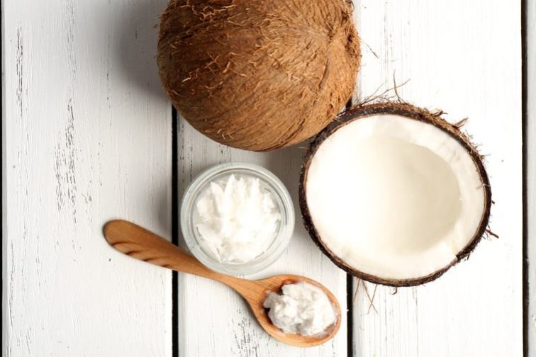 Coconut cut in half laying on white boards with a jar of oil and wooden spoon