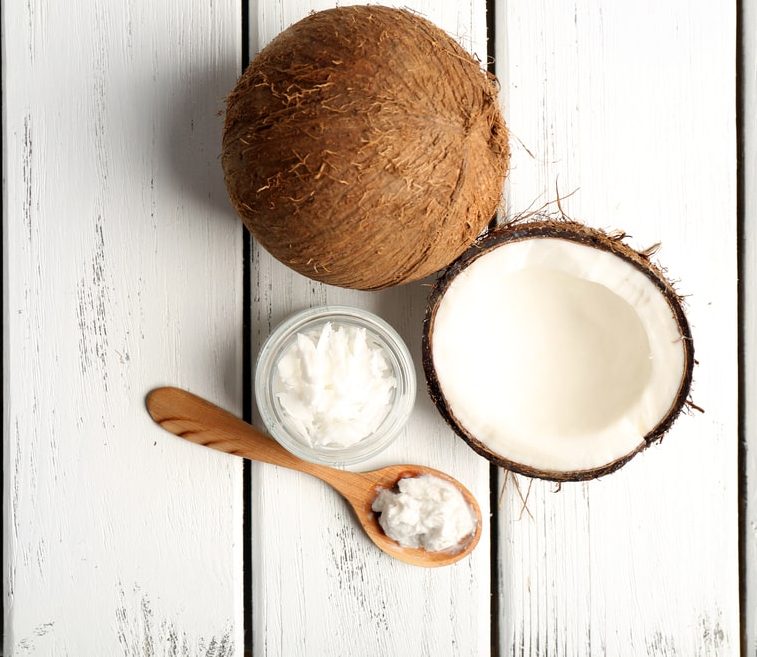 Coconut cut in half laying on white boards with a jar of oil and wooden spoon