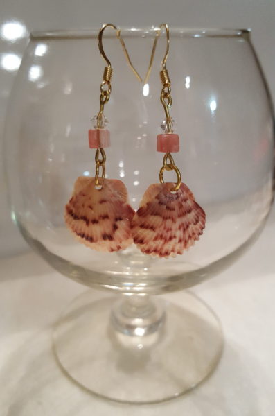 sea shell earrings hanging on rim of glass
