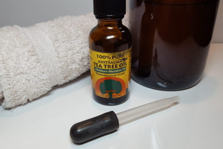 Small bottle of Tea Tree Oil, dropper, brown spray bottle and white cloth
