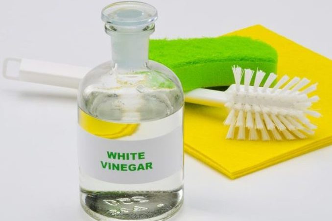 Bottle of White vinegar with scrub brush, green sponge and yellow cloth on white background