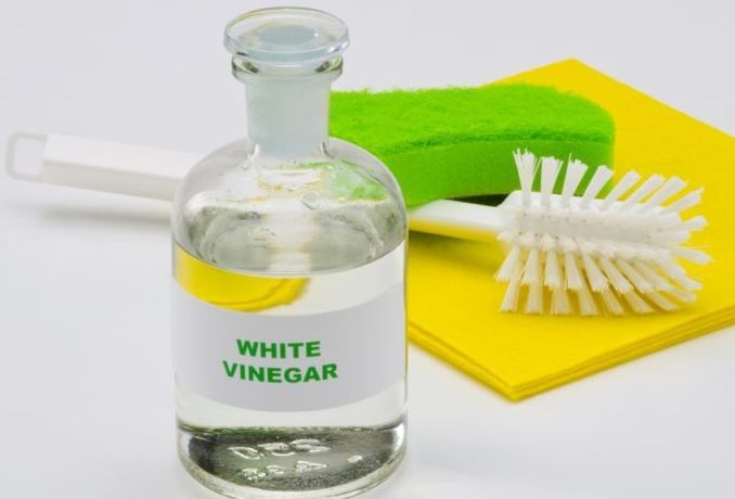 Bottle of White vinegar with scrub brush, green sponge and yellow cloth on white background